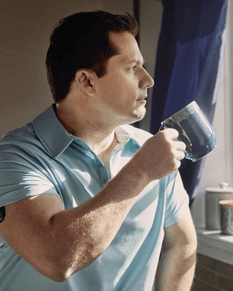 An Eversense CGM user holding a blue mug using the Eversense smart transmitter on his arm